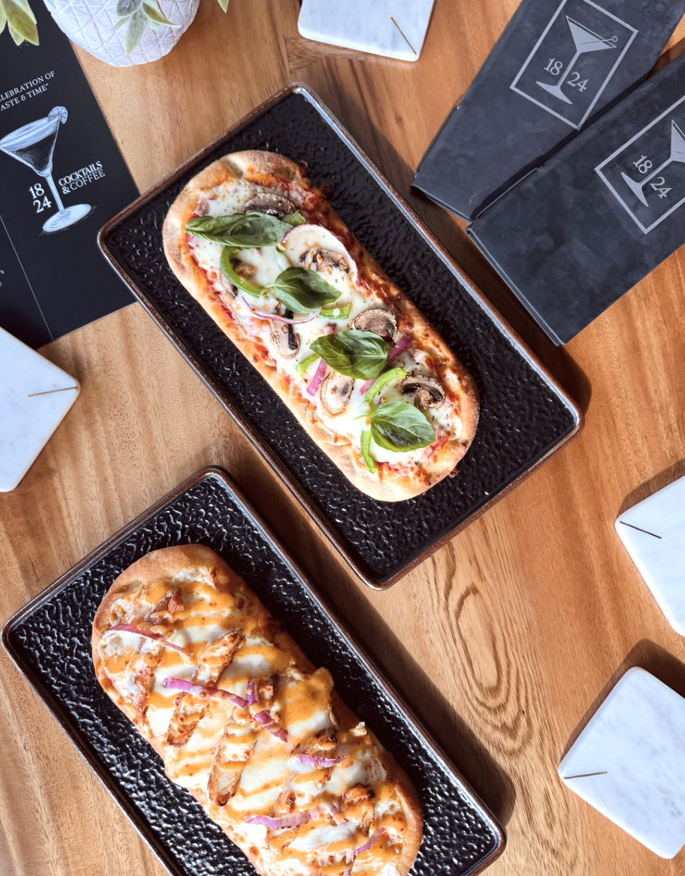Veggie and buffalo chicken flatbreads on textured slate trays beside 1824 menus