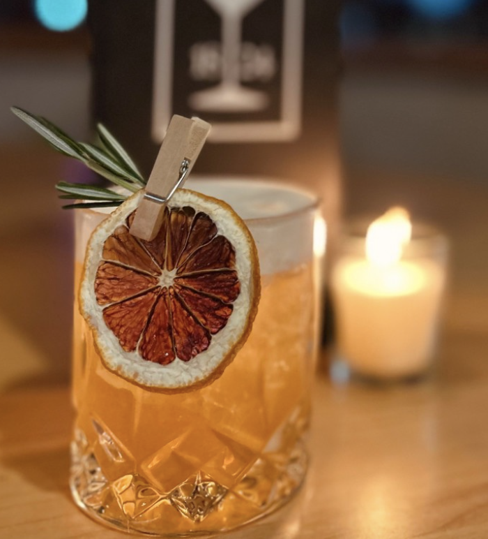 Cocktail garnished with dried citrus and rosemary beside a candle